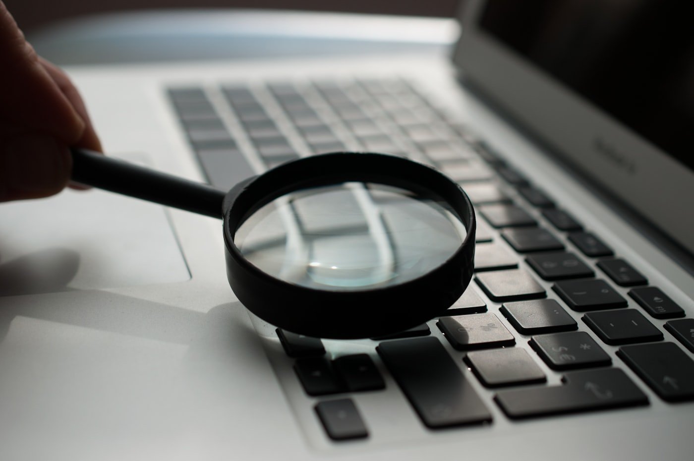 A magnifying glass held over a laptop keyboard, representing careful review and audit